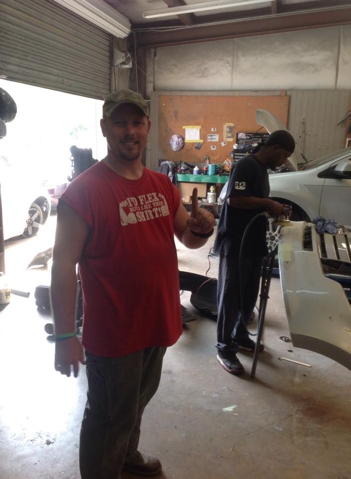 A man in a red shirt is giving a thumbs up in a garage