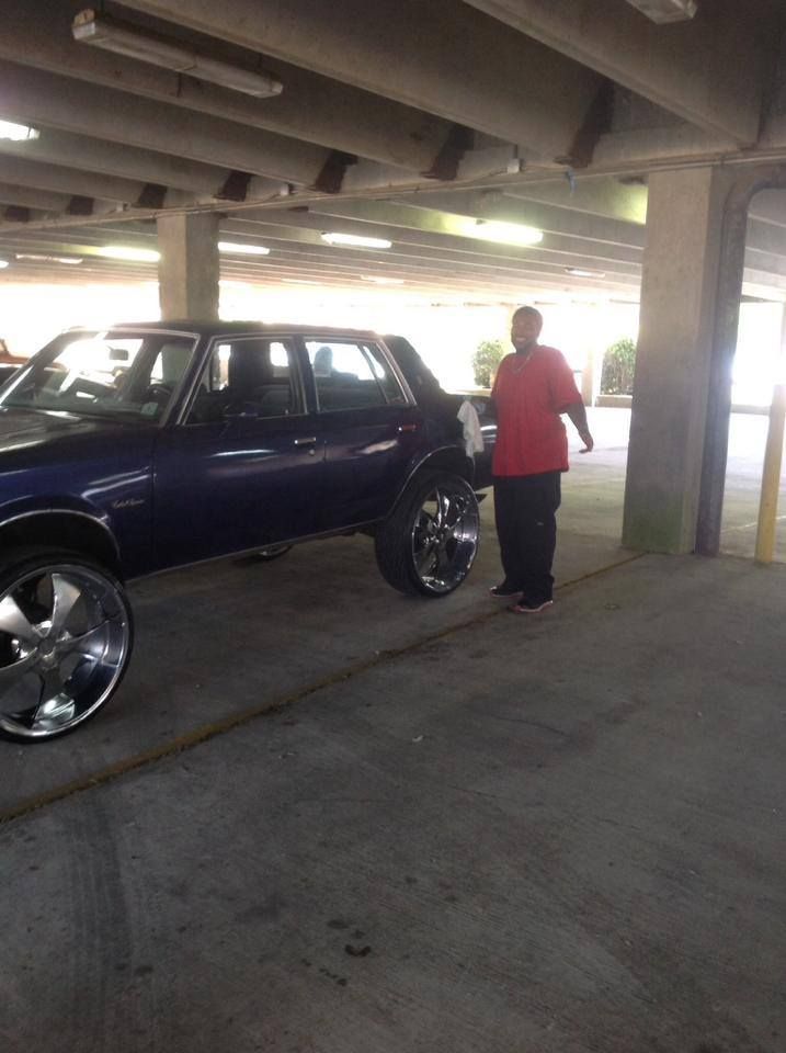 A man in a red shirt is standing next to a blue car in a parking garage