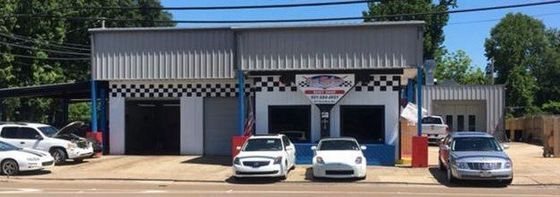 A row of cars are parked in front of a car repair shop.