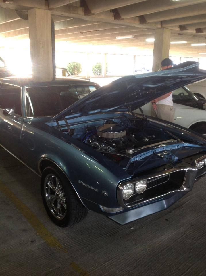 A blue car with the hood up is parked in a parking garage.