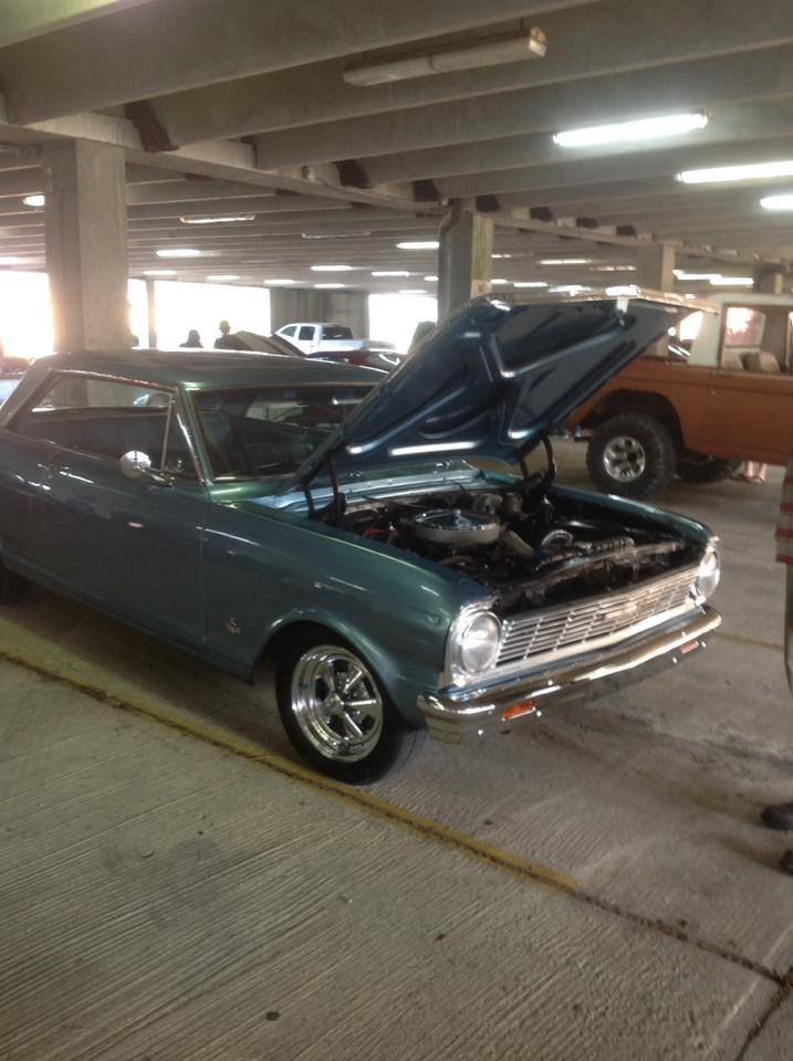 A blue car with the hood up is parked in a parking garage