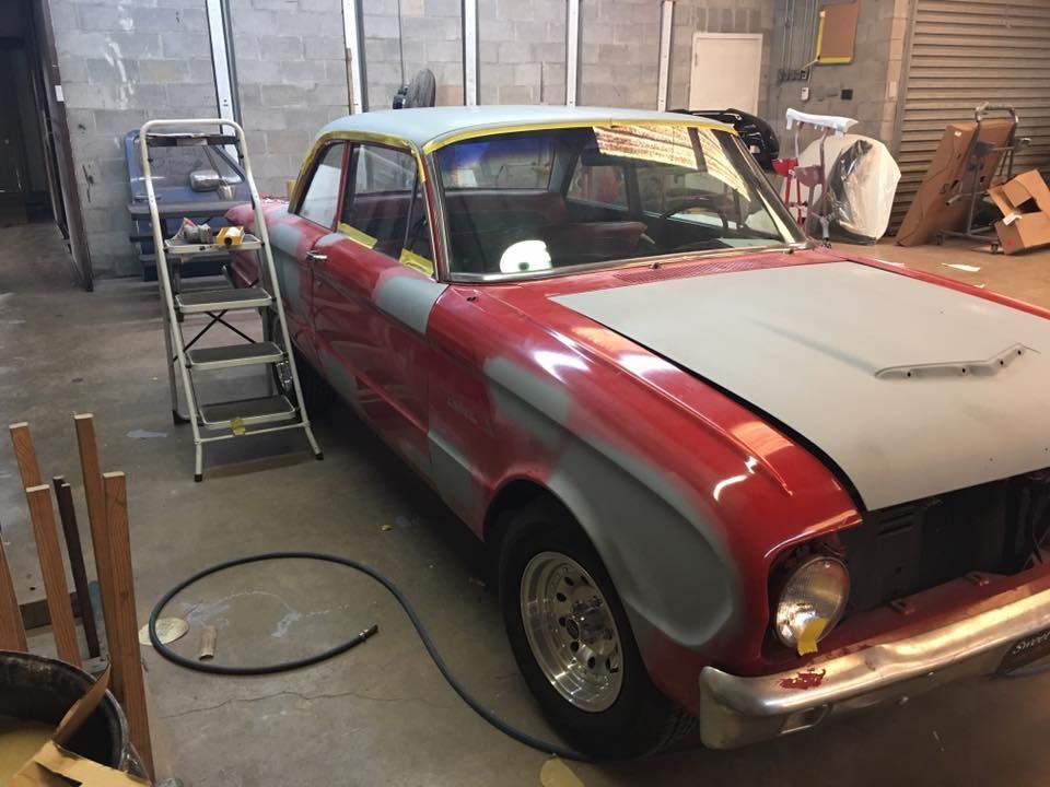 A red car is sitting in a garage with a ladder next to it.