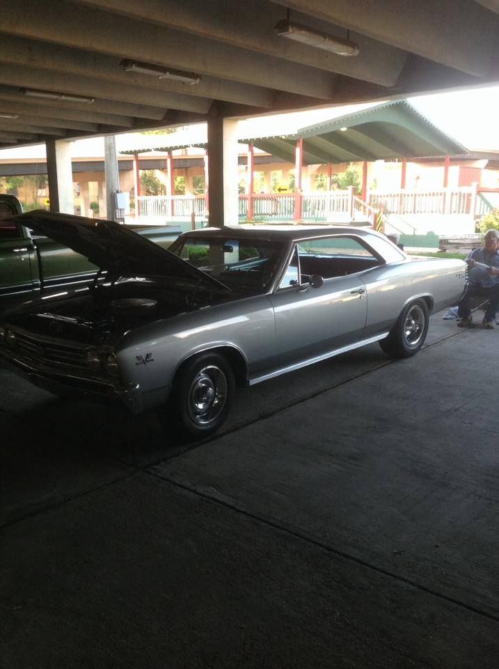 A silver car with the hood up is parked in a parking garage
