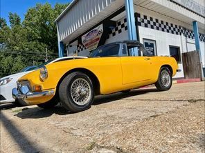 A yellow sports car is parked in front of a car dealership.