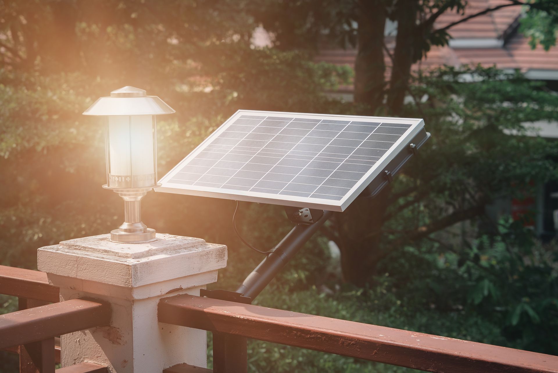 Solar panel mounted on a railing beside a glowing garden lamp at sunset.