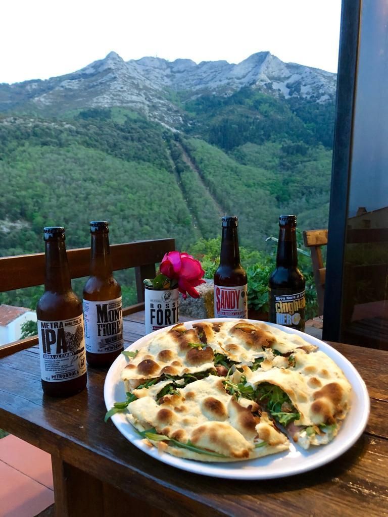 Pizza su un tavolo con bottiglie di birra, con vista su un verde paesaggio montano.