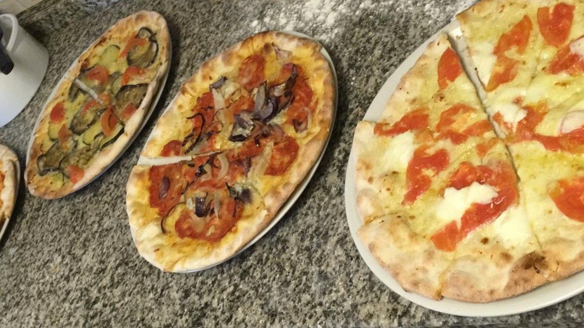 Tre pizze ovali su un piano di lavoro, condite con verdure, formaggio e pomodori.