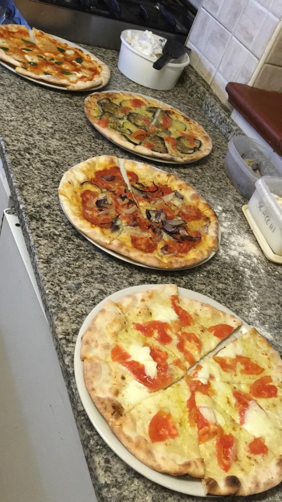 Diverse pizze su un bancone di granito, con un piatto bianco e un contenitore per la salsa sullo sfondo.
