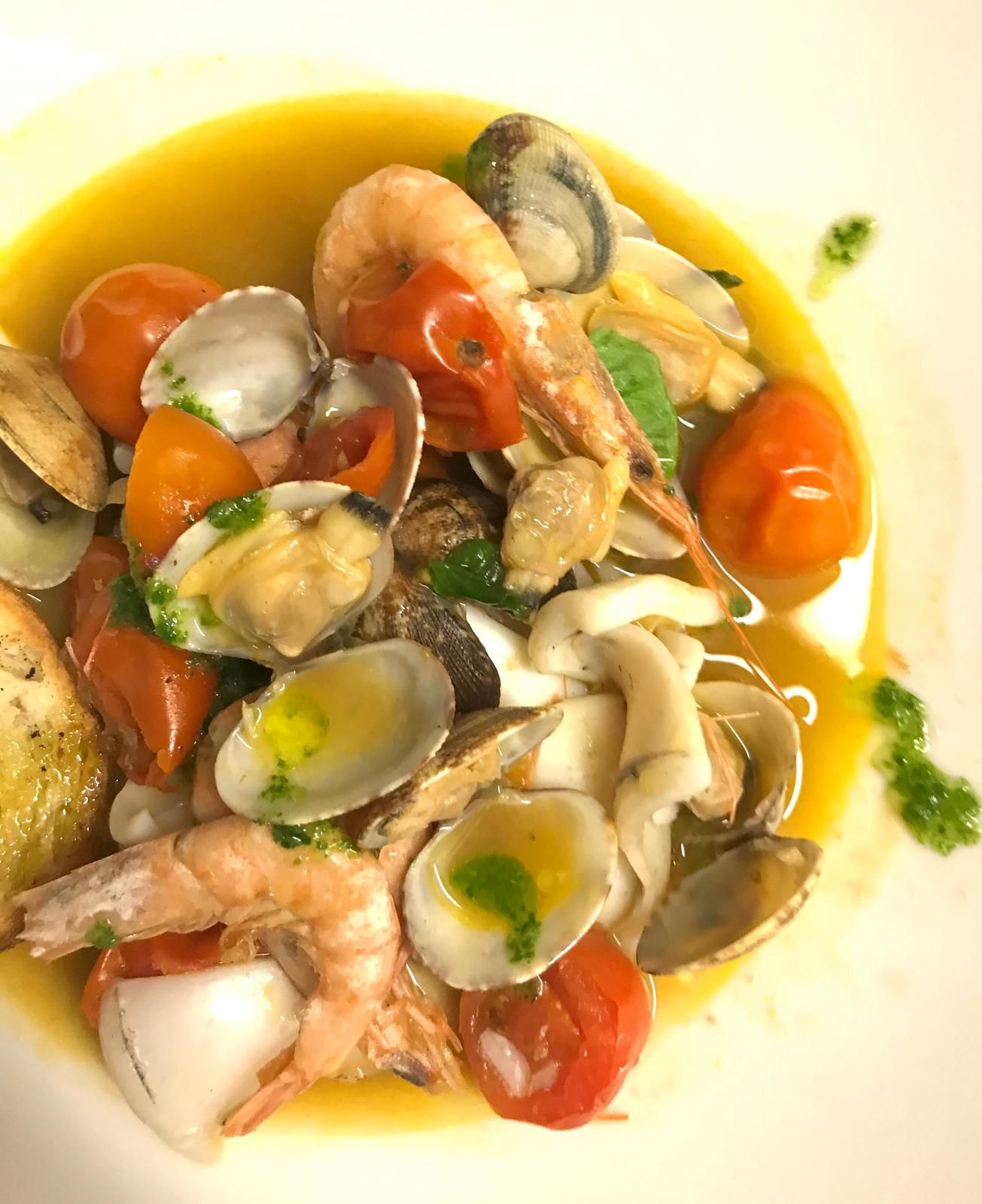 Misto di frutti di mare con gamberi, vongole, pomodori ed erbe aromatiche in una salsa leggera, servito su un piatto bianco.