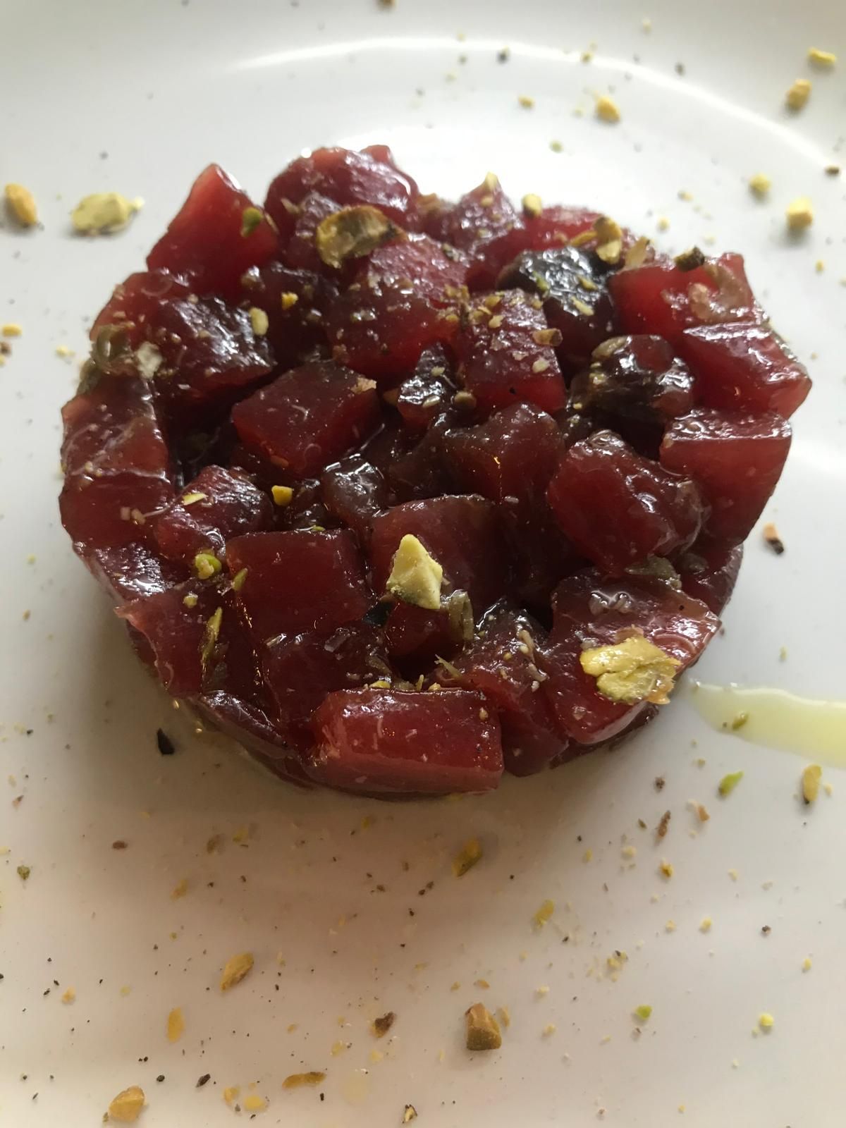 Insalata di barbabietole rosso scuro a dadini in uno stampo rotondo su un piatto bianco, cosparsa di erbe aromatiche e briciole.
