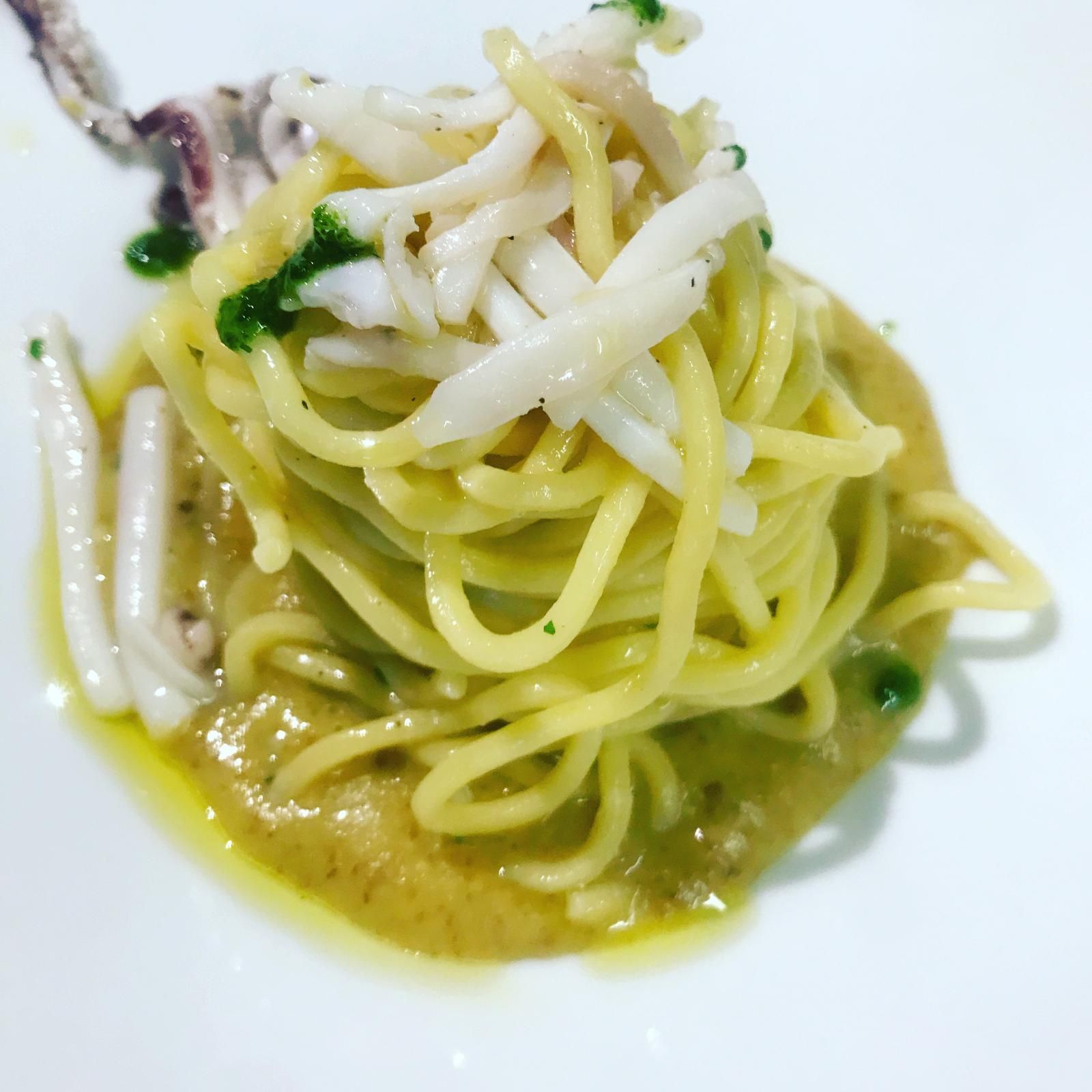 Una piccola porzione di spaghetti con pezzi di frutti di mare bianchi ed erbe aromatiche su un piatto bianco.