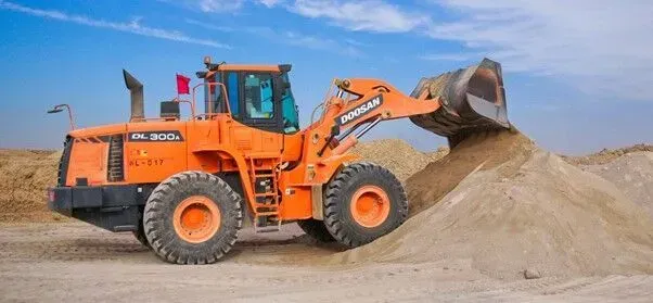 Uma escavadeira está carregando areia em uma pilha em um canteiro de obras.
