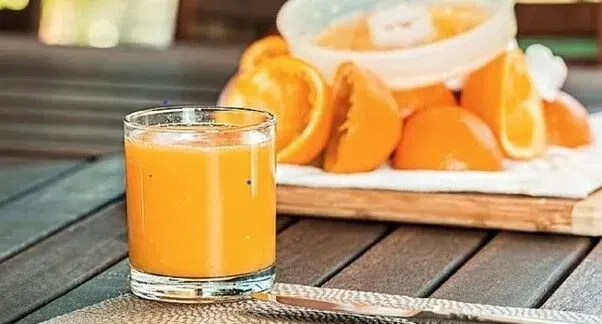 Um copo de suco de laranja está sobre uma mesa de madeira ao lado de laranjas.