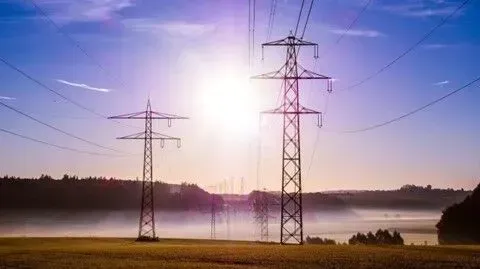 Algumas linhas de energia em um campo com o sol brilhando através delas.