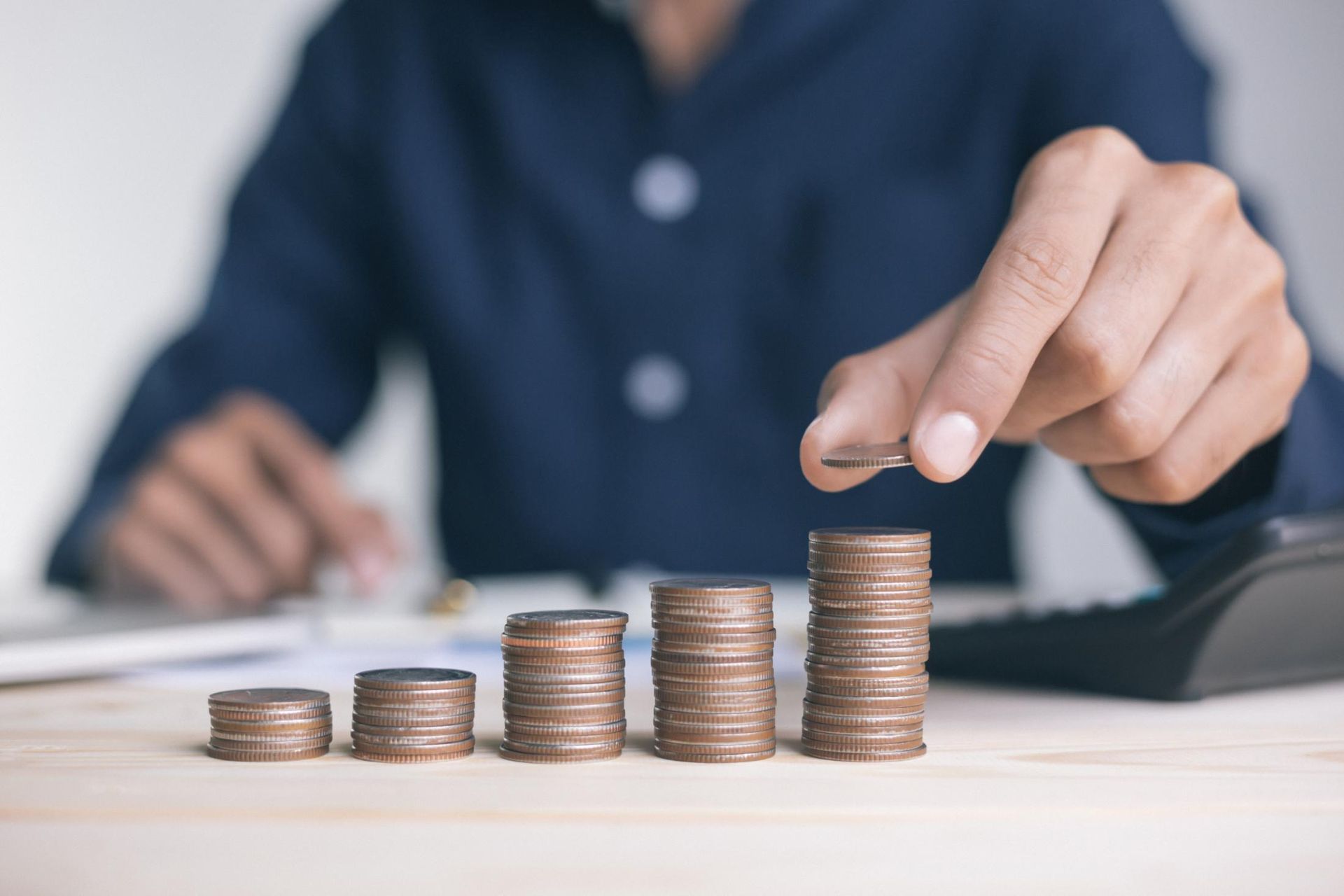 Person stacking coins, creating a growing stack; desk with calculator.