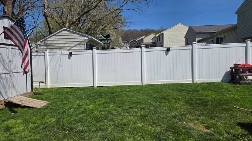 Backyard with green grass, white vinyl fence, and American flag beside a house under a blue sky