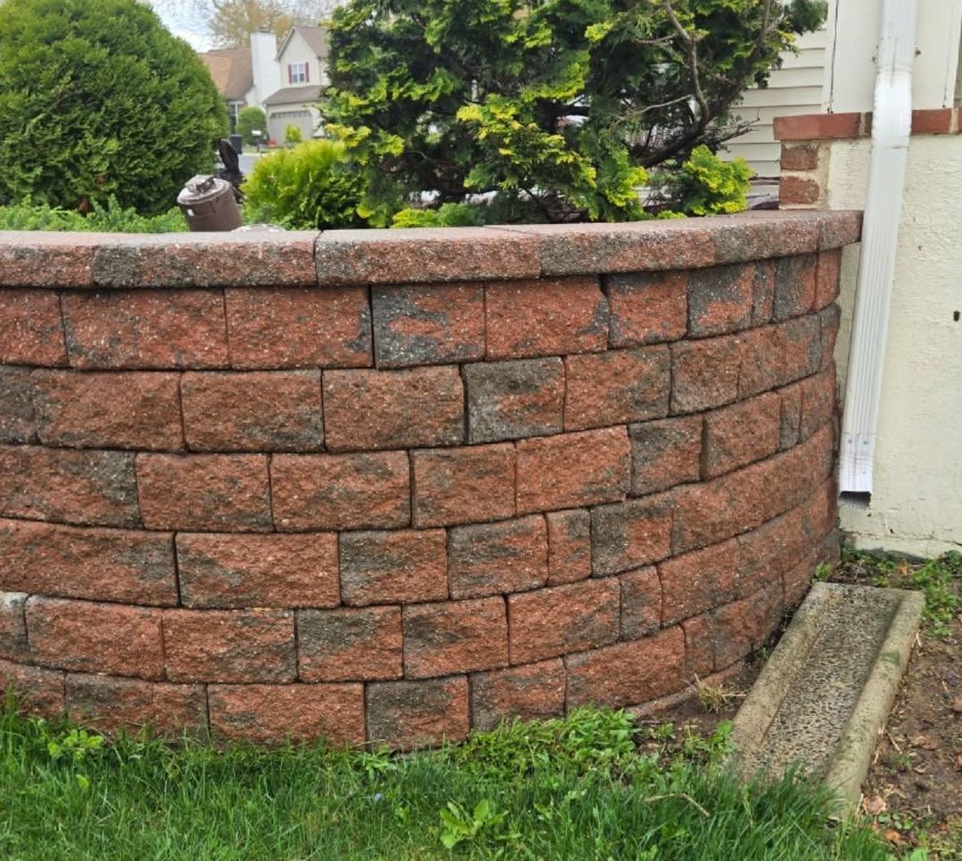 Curved red stone retaining wall beside a grassy yard and driveway