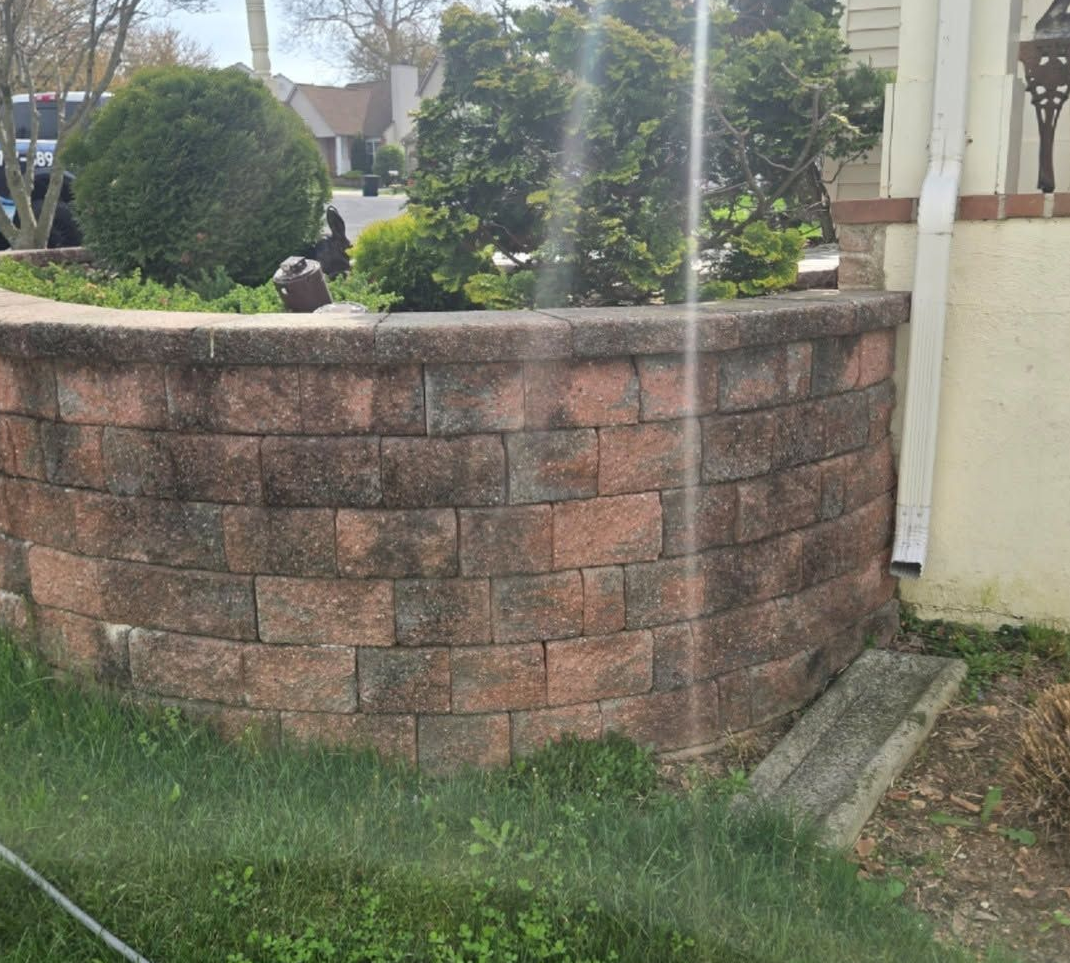 Curved red-brick retaining wall with shrubs in a front yard beside a sidewalk