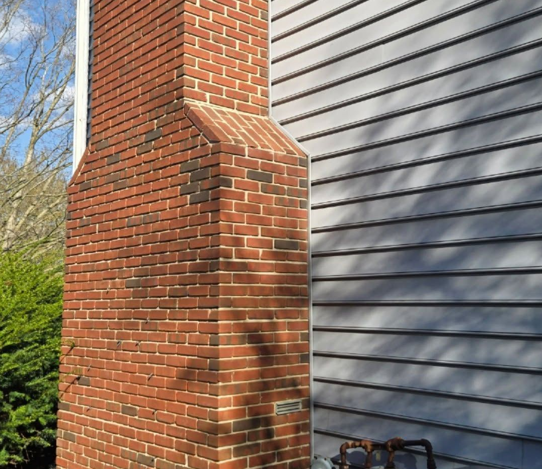 Brick chimney beside gray vinyl siding on a house exterior