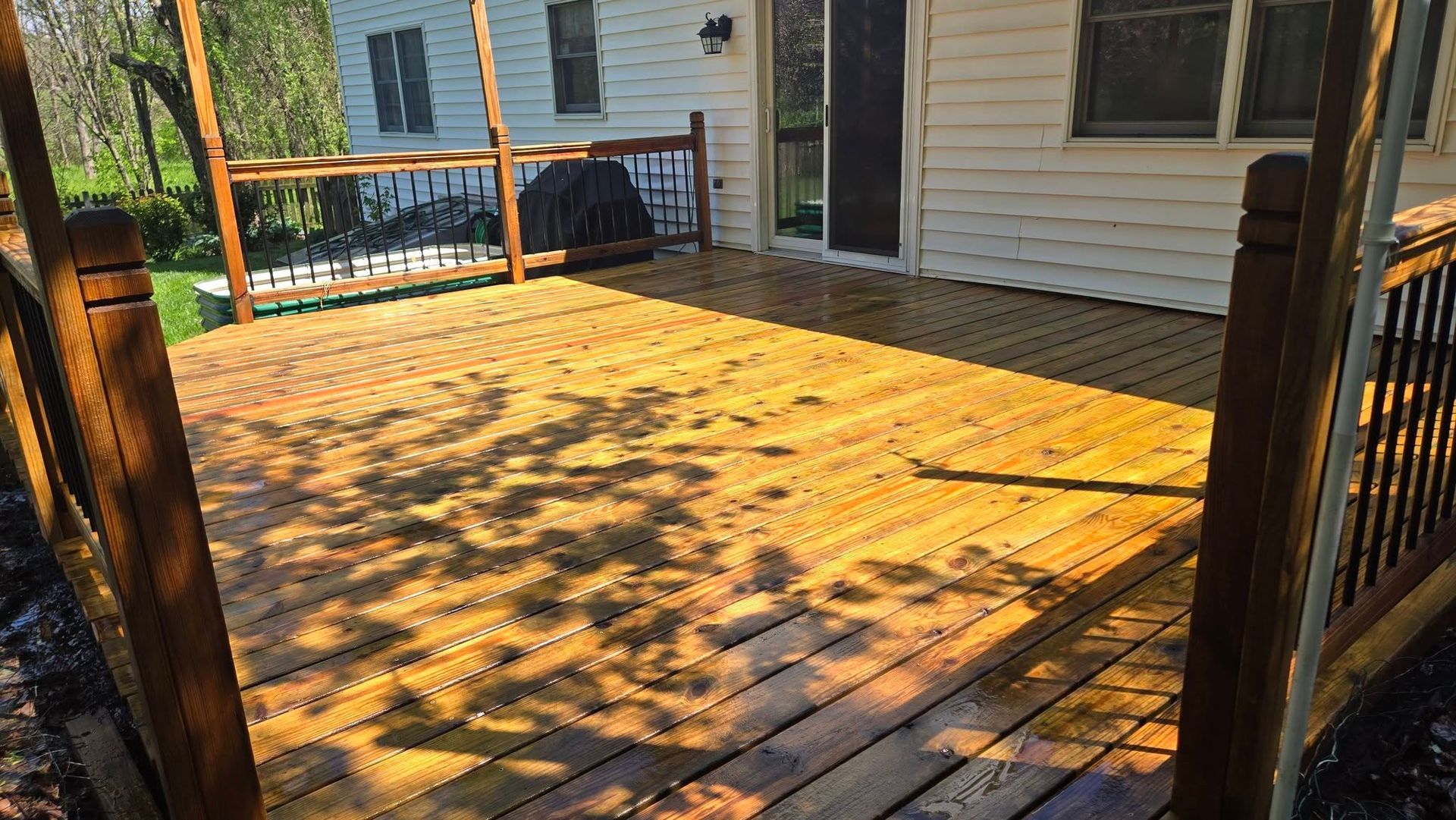 Sunlit wooden deck with railings and a house in the background.