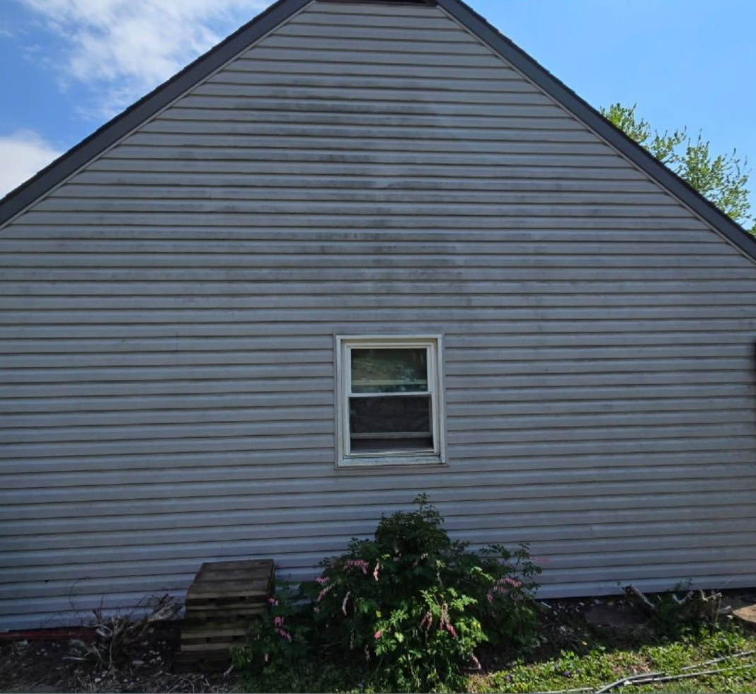 Side view of a gray-sided house with a small centered window and shrubs in front