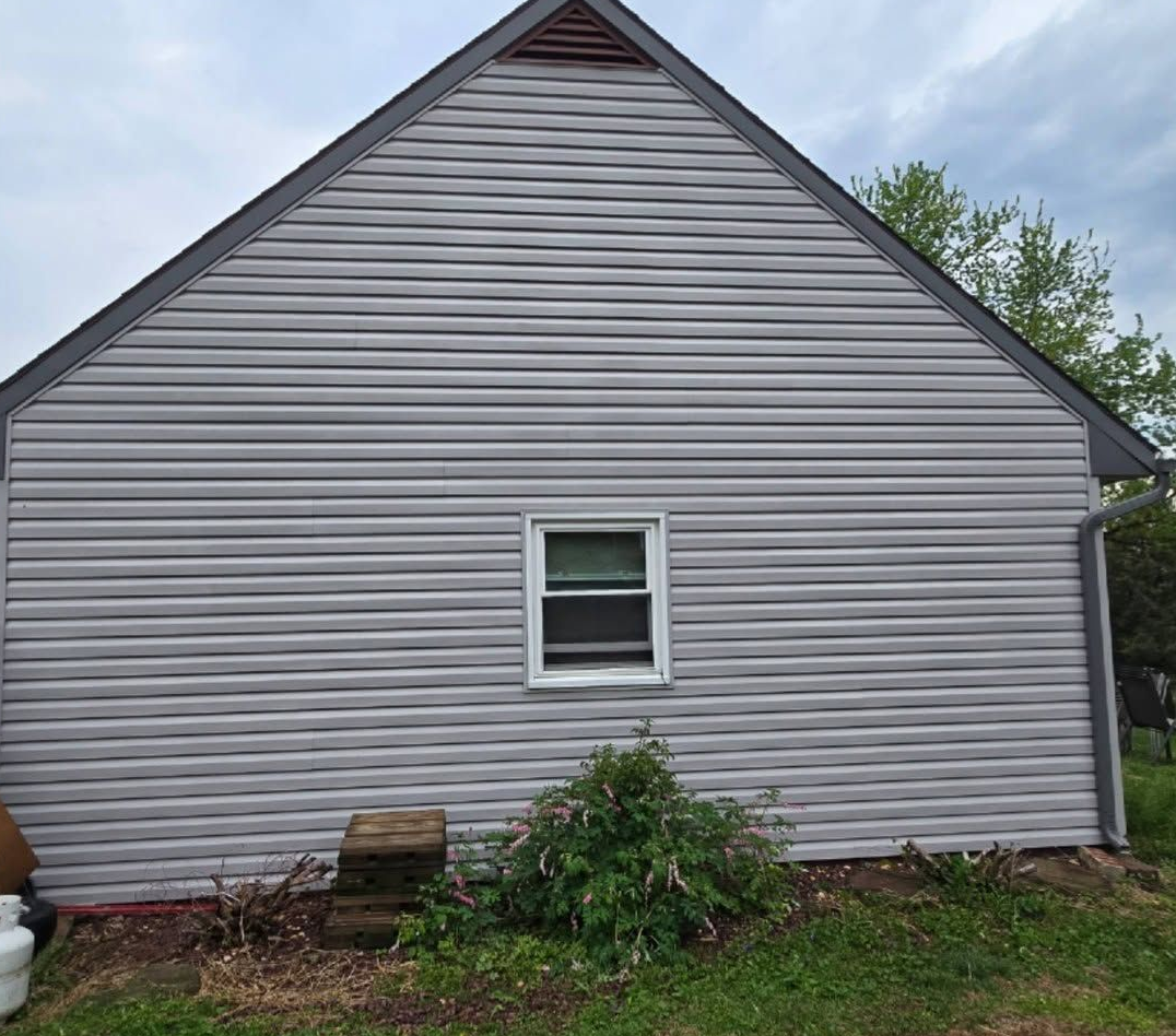 Gray-sided house with a steep roof and one small window, viewed from the yard.