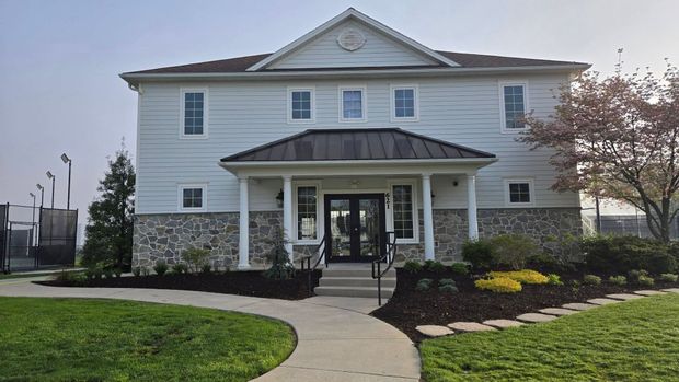 White two-story house with stone accents, a front porch, and a curved walkway in a landscaped yard.