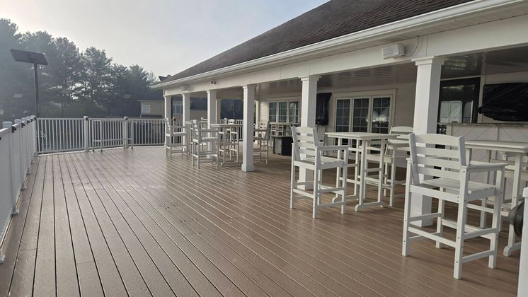Empty wooden deck with white tables and chairs outside a covered building on a foggy day