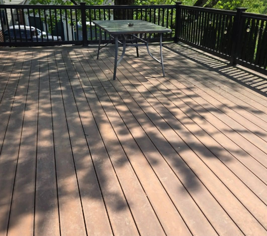 Wooden deck with railings, a patio table, and dappled sunlight and shadows.