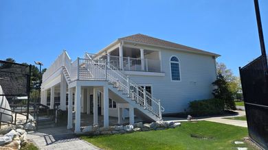White elevated house with exterior stairs and a balcony on a sunny day
