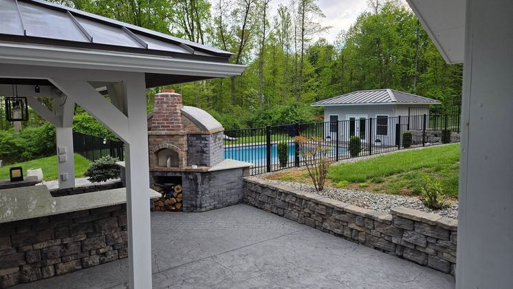 Backyard patio with stone fireplace, pool, and white gazebo surrounded by trees