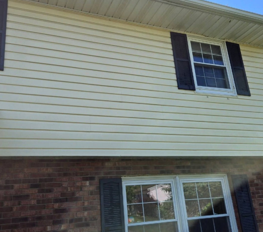 Suburban house exterior with beige siding, brick lower wall, and a window with black shutters.