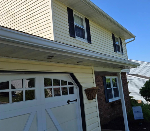 Suburban house exterior with white garage door, beige siding, black shutters, and a small porch lantern