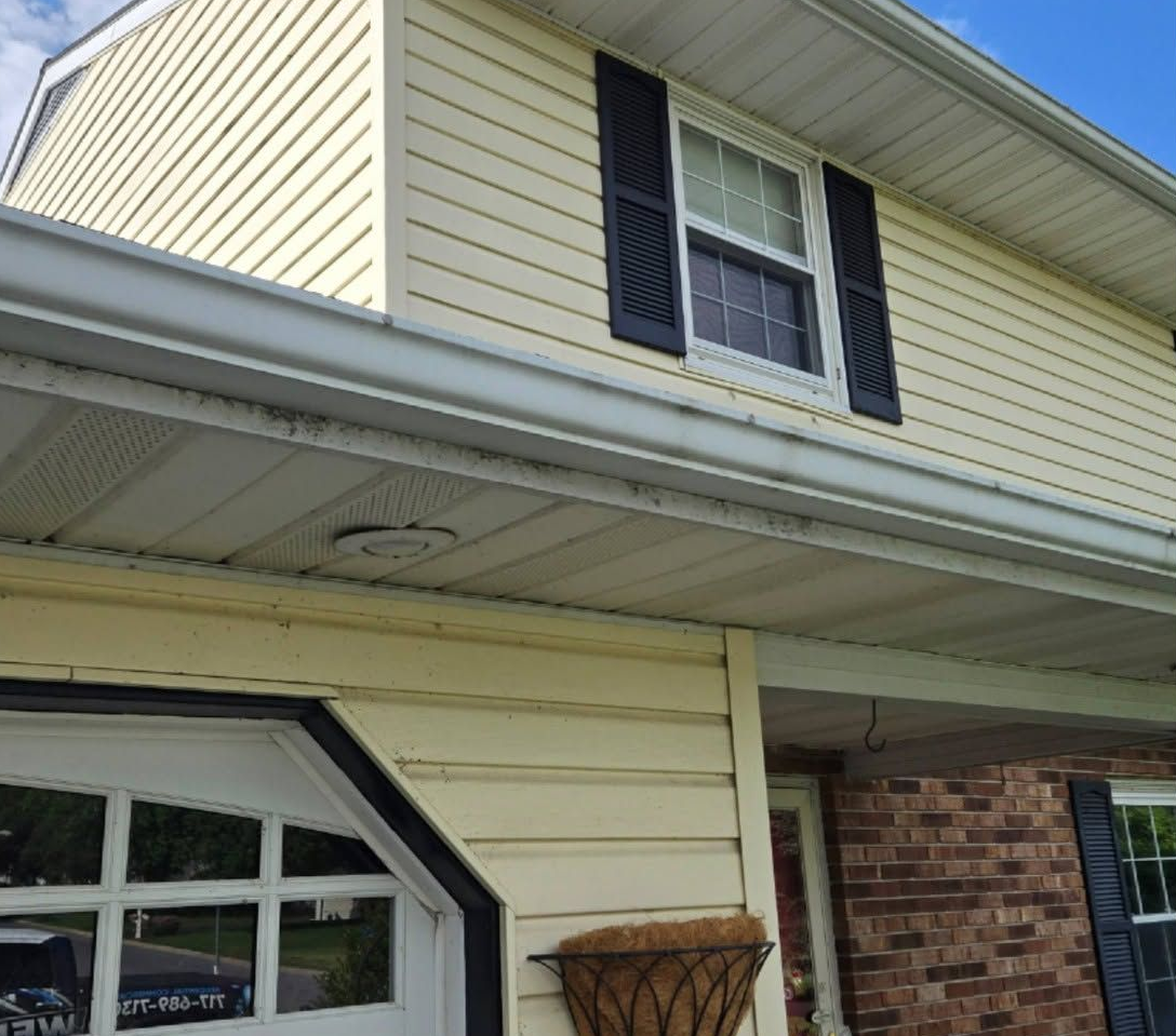 Two-story yellow house exterior with black shutters, brick siding, and a garage door under the eaves