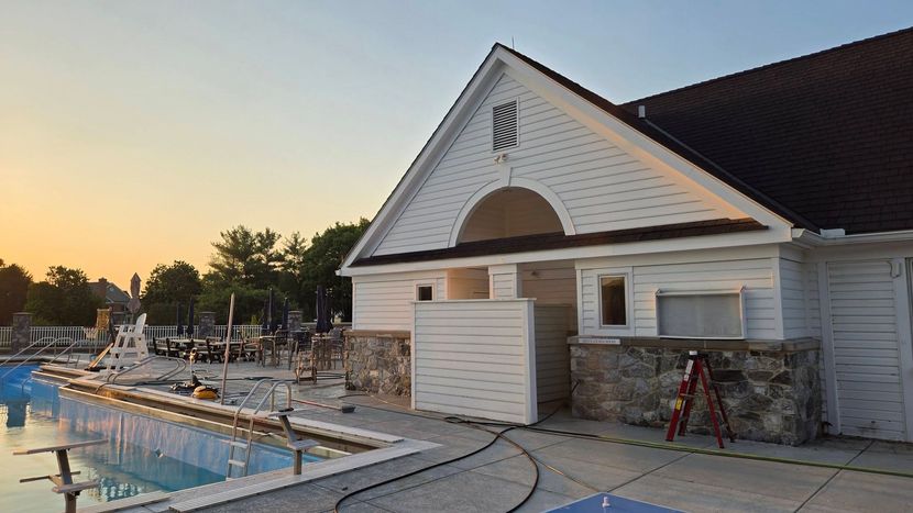 Poolside building under construction at sunset, with white siding, scaffolding, and a swimming pool in front