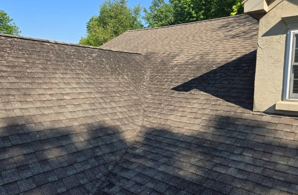 Shingled roof with shadows and a dormer window under a clear blue sky