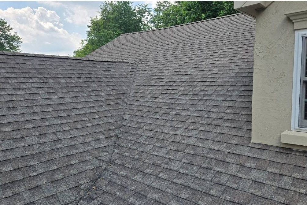 Gray shingled roof with a dormer and beige siding under a cloudy sky