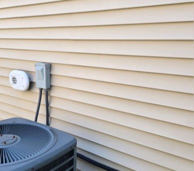 Outdoor HVAC unit and wall-mounted utility boxes beside beige house siding