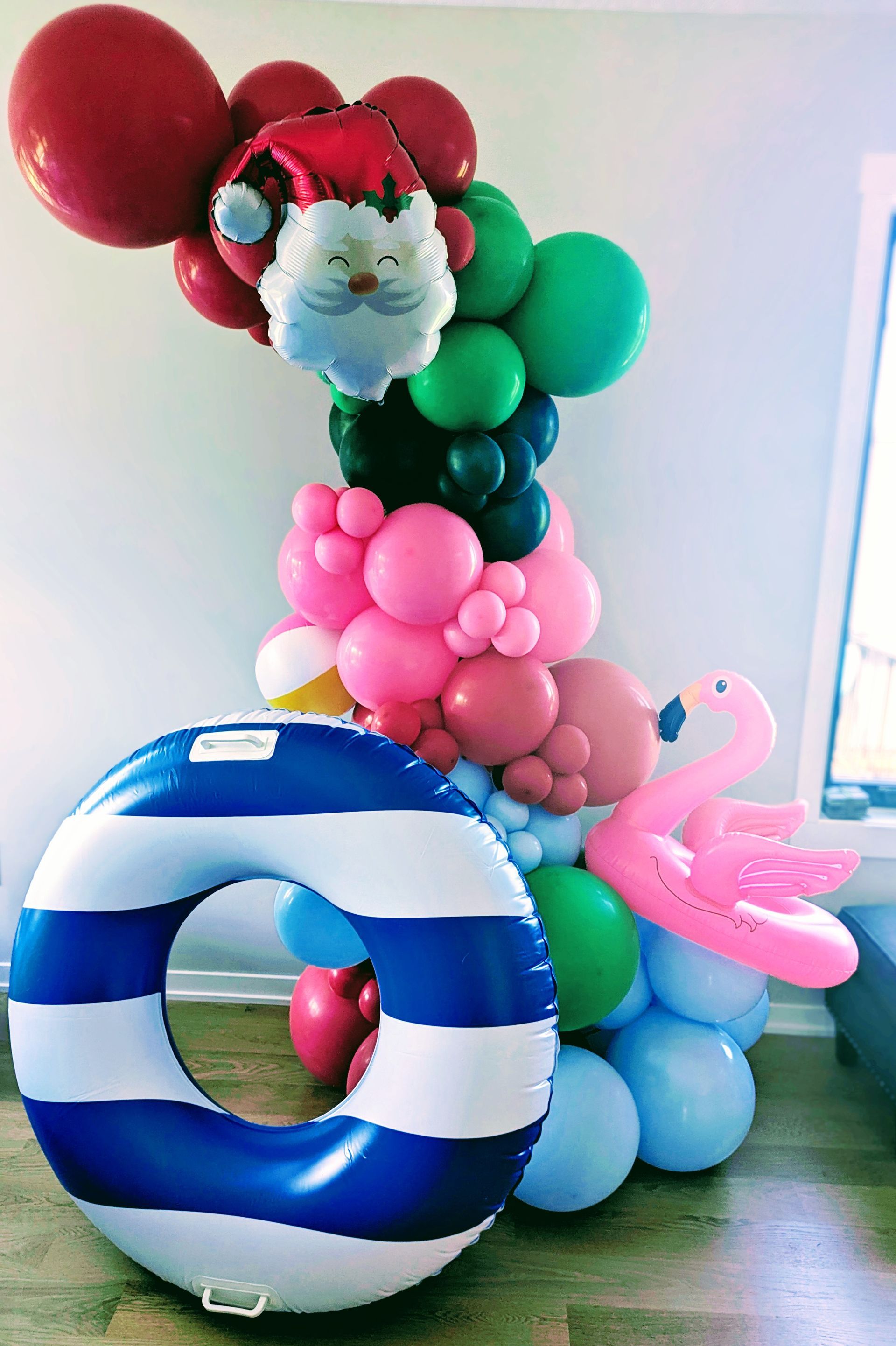 A festive balloon arch with a Santa, beach elements, and a blue and white striped inflatable ring.
