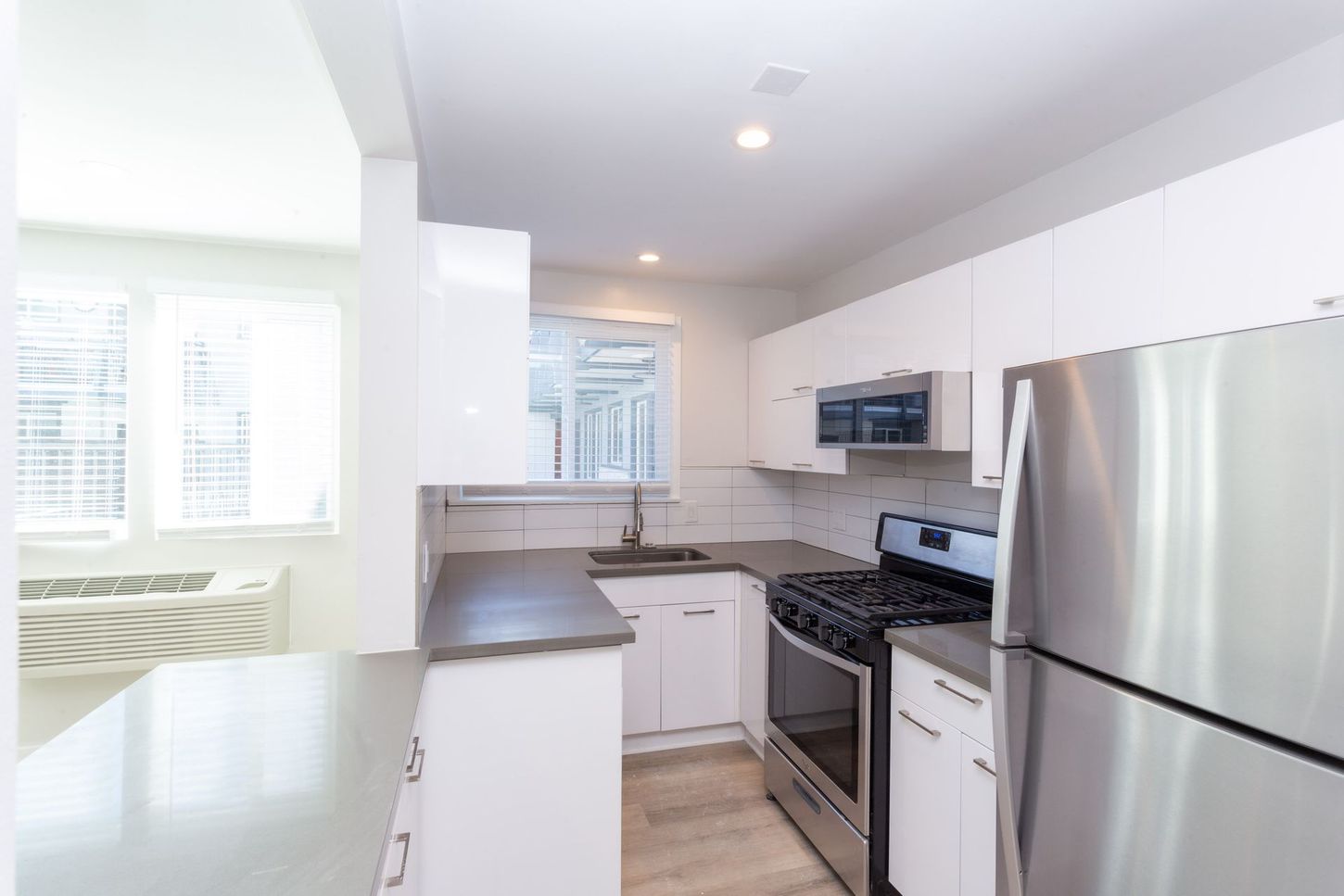 Bright modern kitchen with stainless steel appliances, white cabinets, and a breakfast bar by the windows