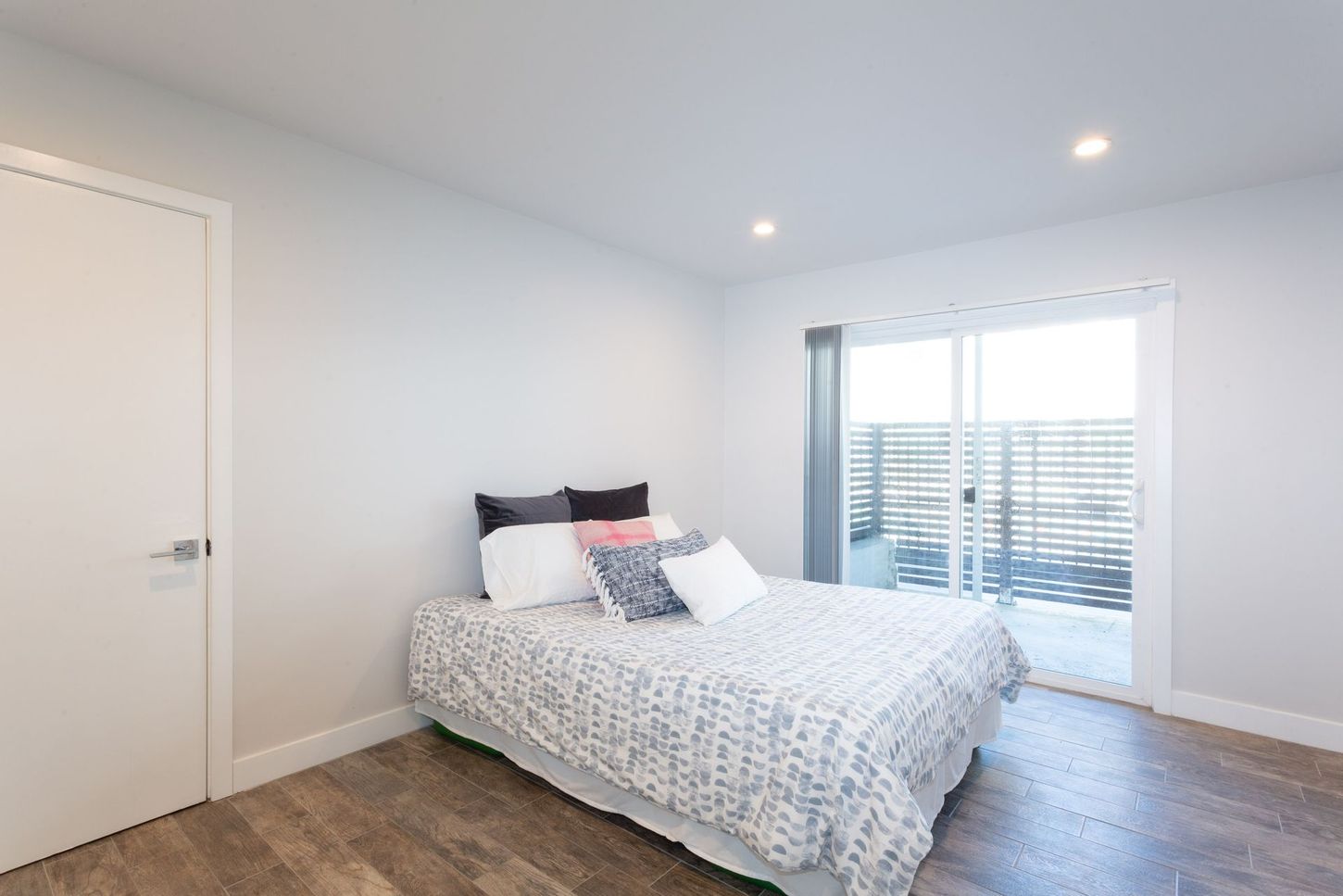 Bright bedroom with a bed, white walls, wood floor, and window blinds.