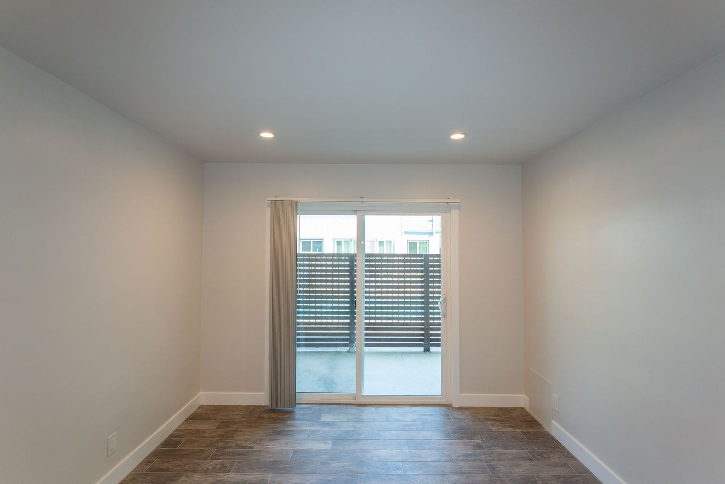 Empty white room with recessed lights, wood floor, and sliding glass doors to a balcony