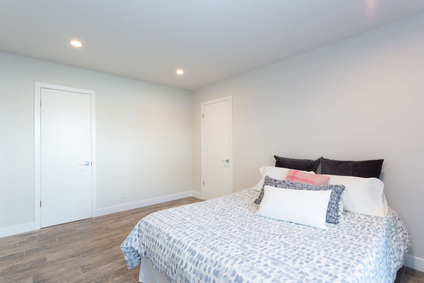 Bright bedroom with a bed, white walls, two closed doors, and wood flooring