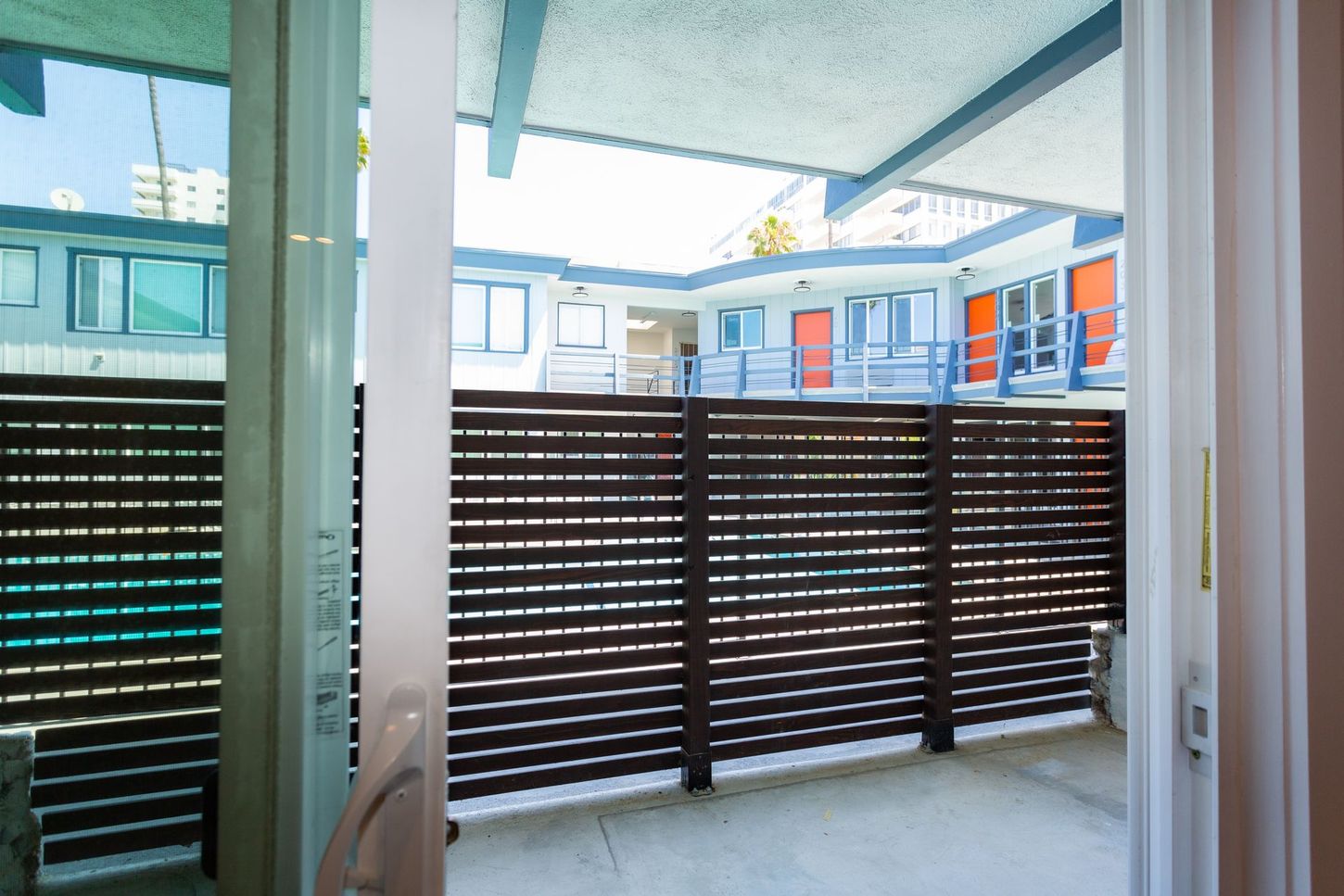 Balcony view with a dark slatted privacy screen and neighboring buildings in bright daylight