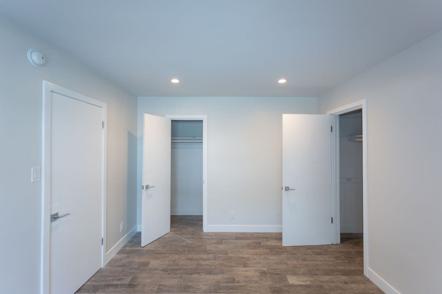 Empty white bedroom with carpet, recessed lights, and two open closet doors