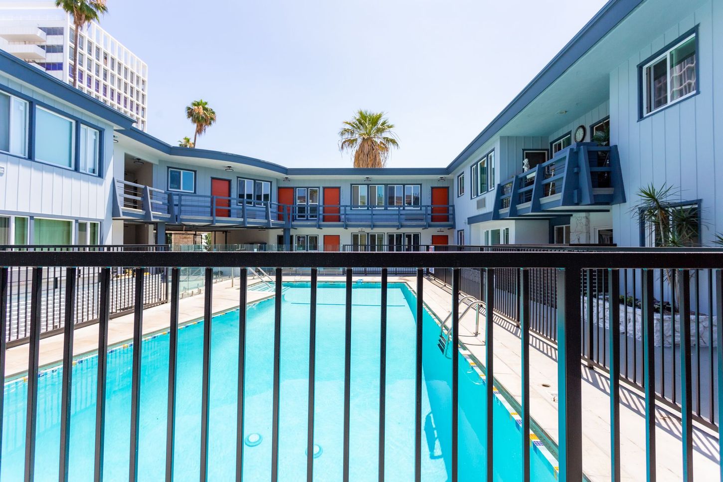 Apartment courtyard with a turquoise pool, black railing, and modern blue-and-white buildings around it