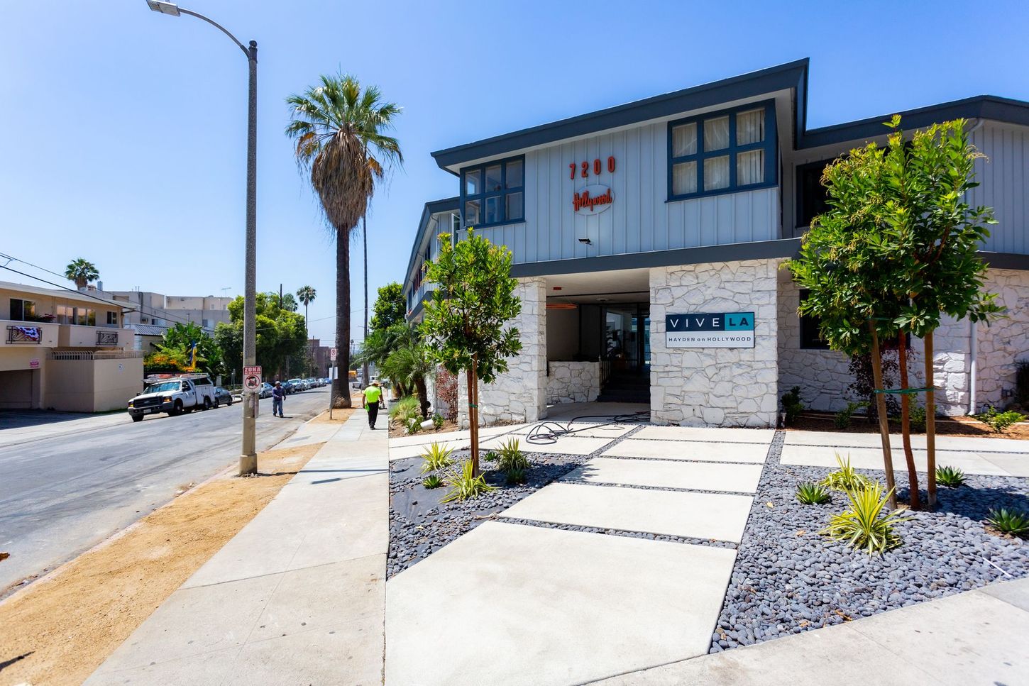 Modern apartment building with white stone facade, palm trees, and a bright sidewalk under a clear sky
