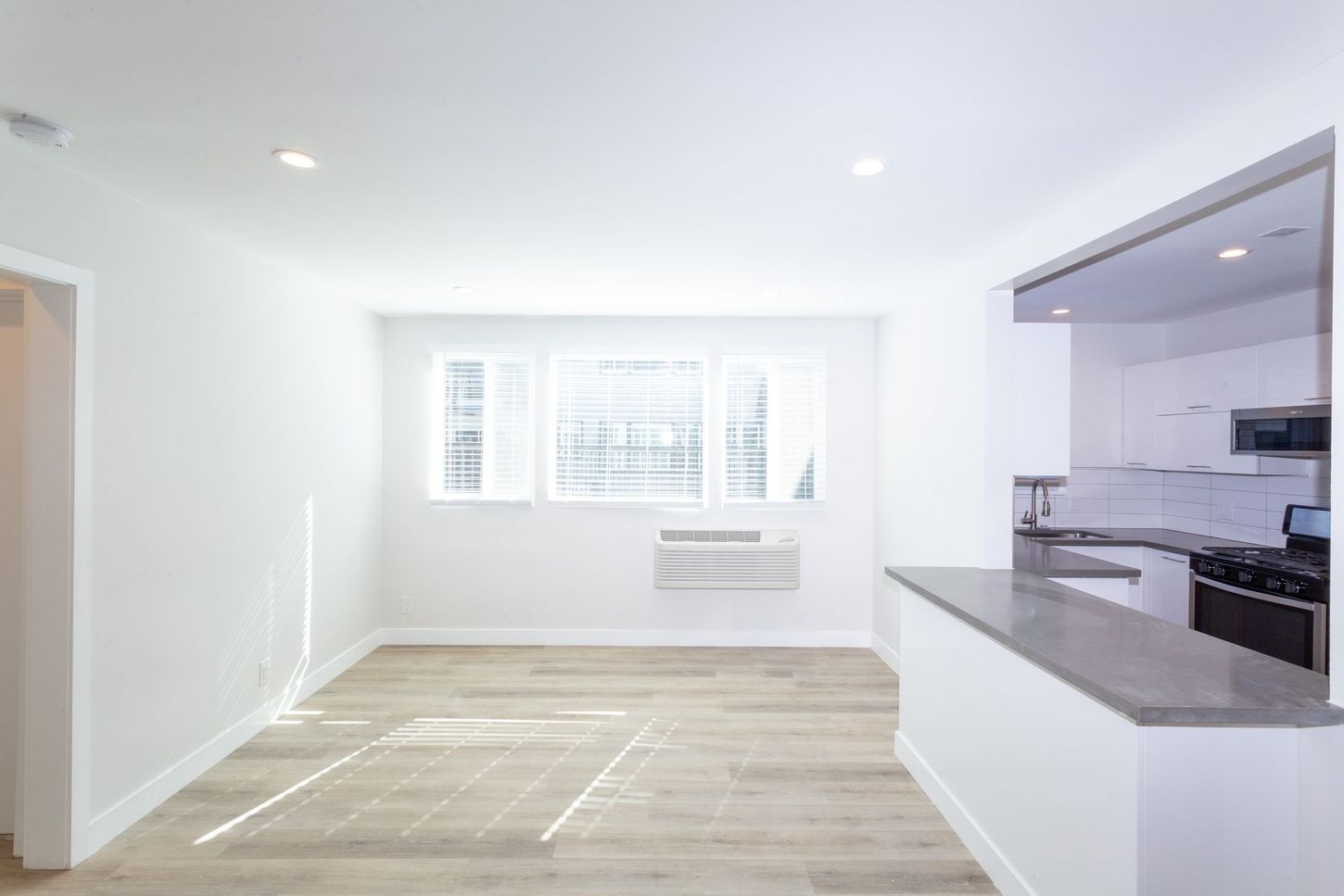Bright empty living room with white walls, wood floors, and open kitchen counter in a modern apartment