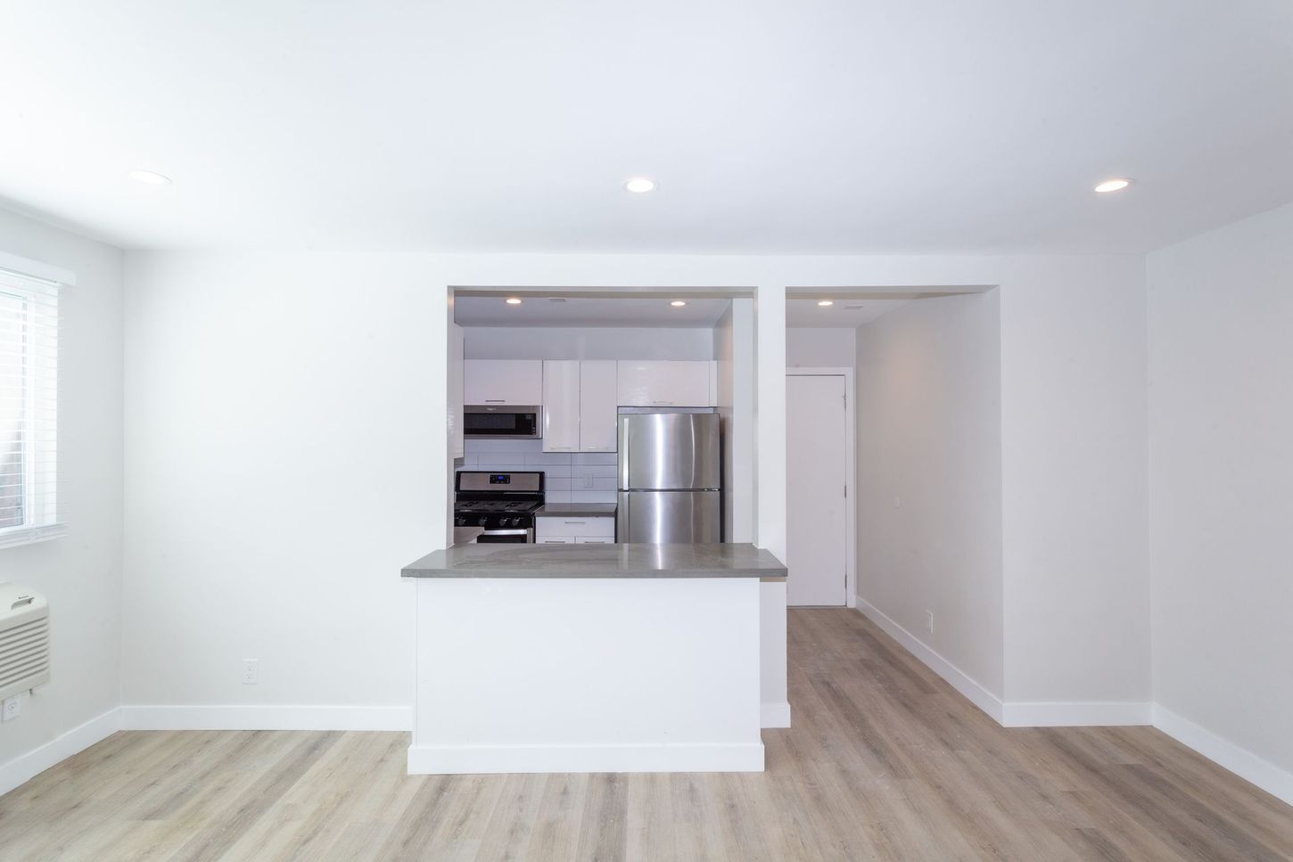 Bright, empty modern kitchen with white walls, wood floors, and a stainless steel refrigerator at a pass-through counter