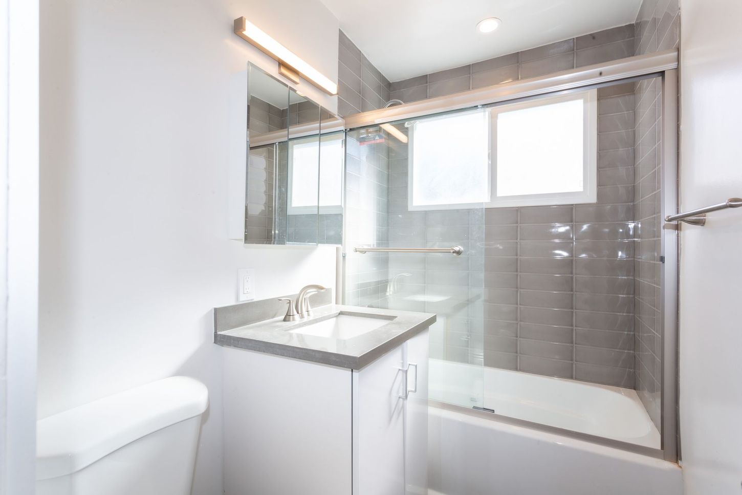Bright modern bathroom with a sink vanity, mirror, window, and glass shower enclosure.
